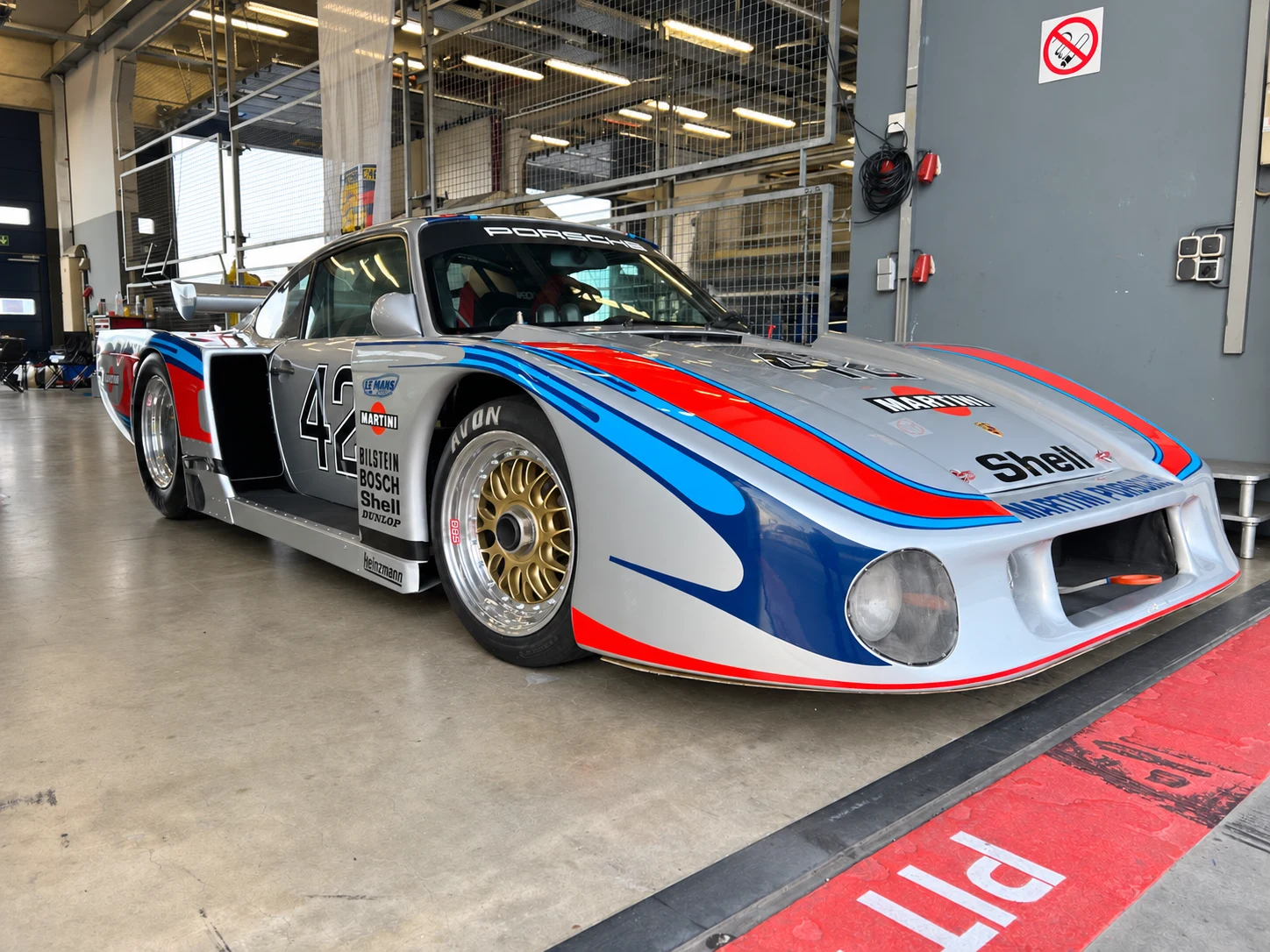 Ezüst Porsche versenyautó piros-kék versenyfestéssel a garázsban