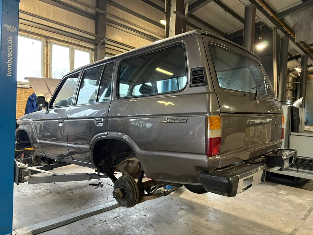 Szürke Land Cruiser emelőn, bal hátulról, leszerelt kerekekkel