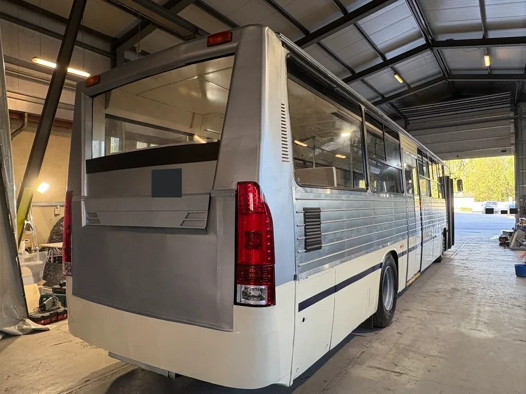 Rear and side of the silver and white converted bus in the workshop