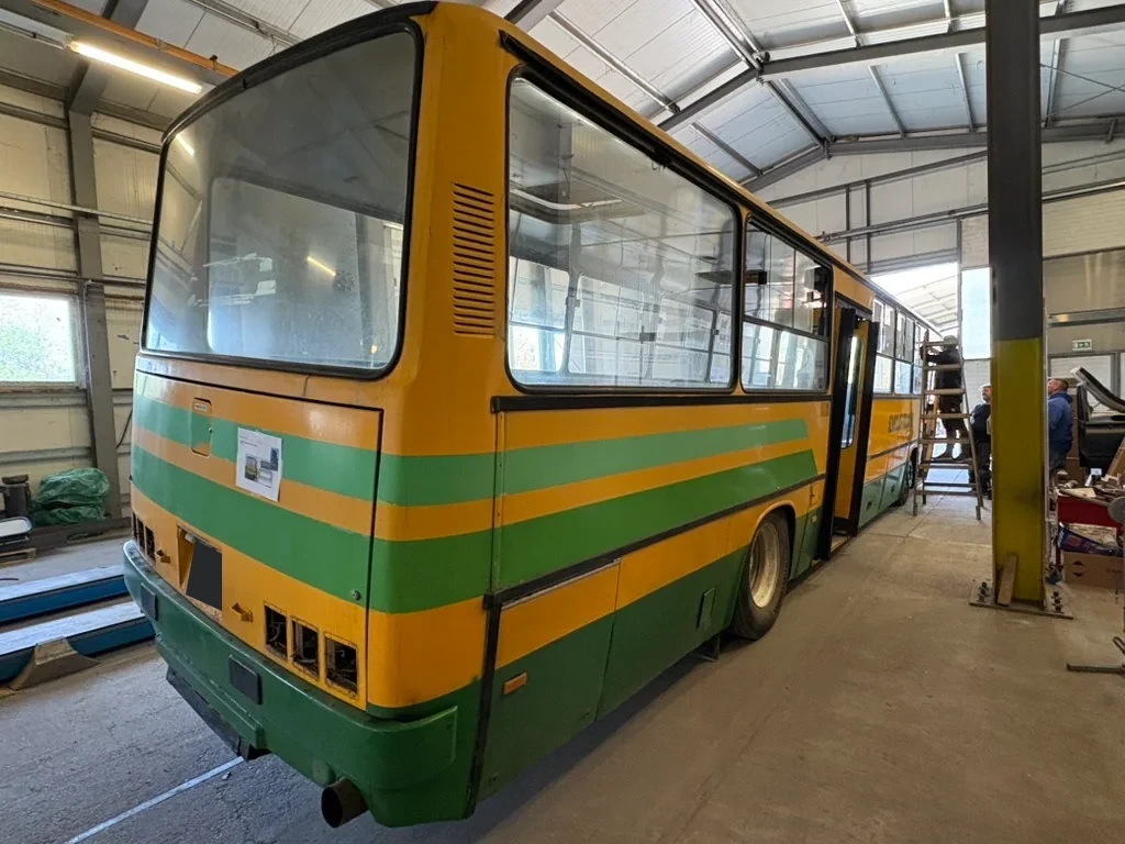 Rear and side of a yellow and green bus in the workshop
