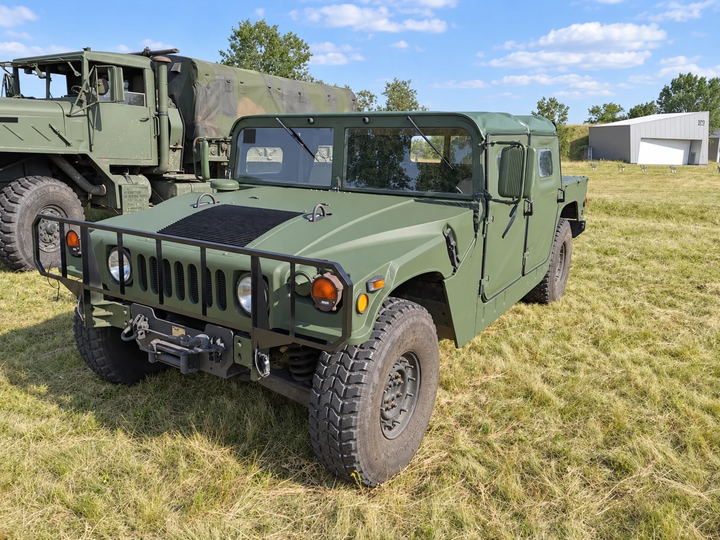 Olajzöld Humvee, háttérben katonai szállítójárművel